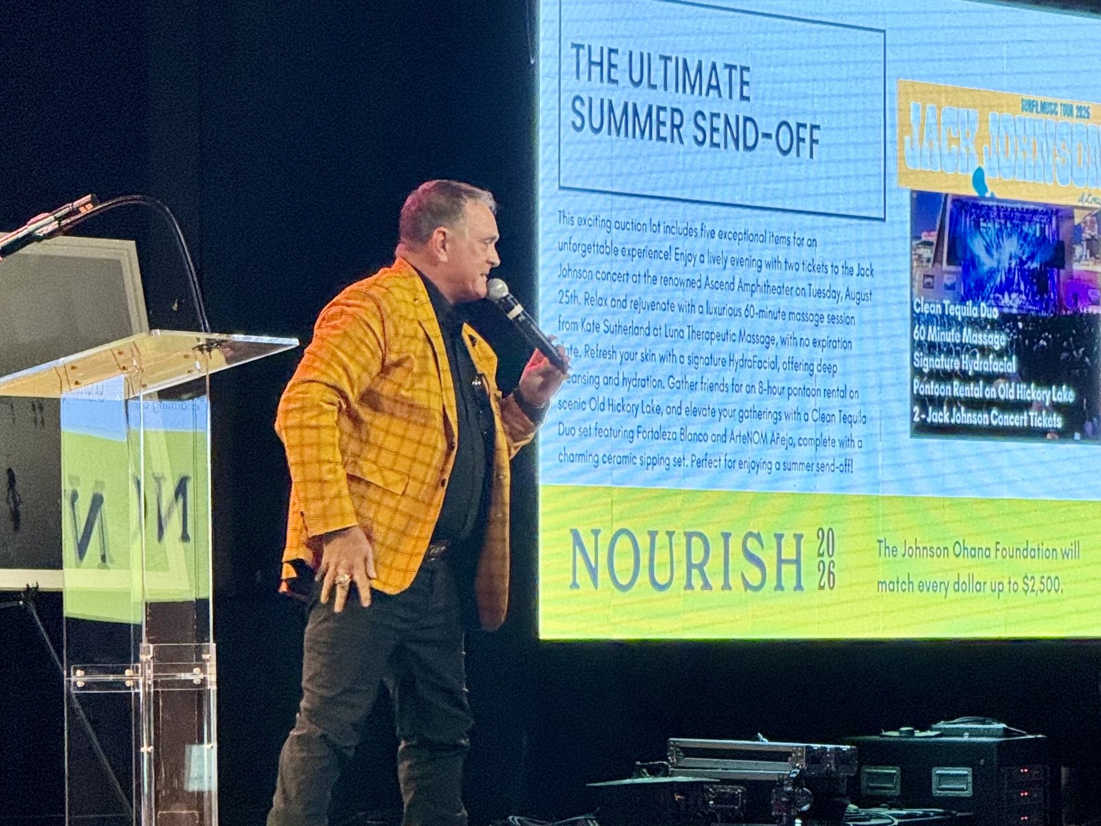 Todd Nichols on stage at NOURISH 2026 calling a live auction lot, with the NOURISH screen behind him