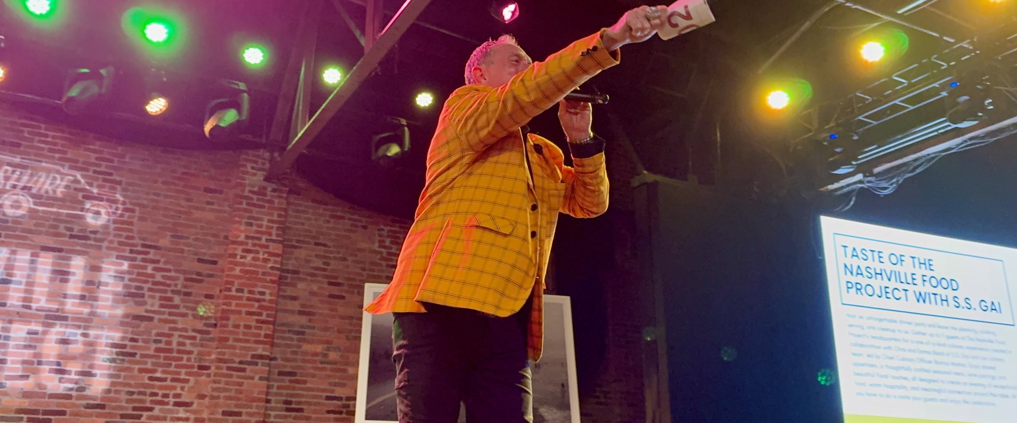 Todd Nichols, bid card raised, calling the fund-a-need on stage at NOURISH 2026